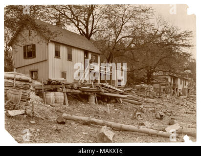 Horizontale, schwarz und weiß Fotografie eine Geschichte zwei seitig Residenz mit Fensterläden. Drei Leute stehen auf der Veranda. Stapel von Holz und Fässer Wurf den Vorgarten. Titel: hausbesetzer der Häuser am Flussufer in Carondelet. Elwood Street, Fuß. . 1895. Swekosky, William G., 1895-1964 Stockfoto