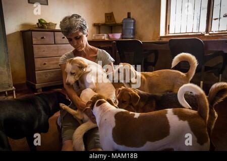 Kandy, Sri Lanka. 21 Feb, 2018. EVA RUPPEL sitzt mit einem kleinen Satz von geretteten Hunde in Ihrer Küche in der Nähe von Kandy, Sri Lanka, am Mittwoch, 21. Februar 2018. Ruppel nicht Käfig die ungefähre 170 geretteten Hunde mit ihr zu leben, die Ihnen Bewegungsfreiheit und interagieren in Kleinpackungen in mehrere Stifte in ihrer Eigenschaft als auch innerhalb Ihres Hauses. Ruppel erstellt Tikiri Vertrauen, mit der finanziellen Unterstützung ihres Vaters, zu retten und rehome Sri Lanka's Street Dogs. Es ist unmöglich, Sri Lanka, ohne zu sehen, Street Dogs in fast jedem öffentlichen Raum zu besuchen, in der Nähe von Hotels, Pensionen Stockfoto