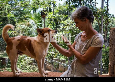 Kandy, Sri Lanka. 21 Feb, 2018. EVA RUPPEL sitzt mit Banyan, einer der 170 Hunde leben mit ihr in der Nähe von Kandy, Sri Lanka, am Mittwoch gerettet, 21. Februar 2018. Ruppel nicht Käfig die Hunde mit ihr zu leben, die Ihnen Bewegungsfreiheit und interagieren in Kleinpackungen in mehrere Stifte in ihrer Eigenschaft als auch innerhalb Ihres Hauses gerettet. Ruppel erstellt Tikiri Vertrauen, mit der finanziellen Unterstützung ihres Vaters, zu retten und rehome Sri Lanka's Street Dogs. Es ist unmöglich, Sri Lanka, ohne zu sehen, Street Dogs in fast jedem öffentlichen Raum zu besuchen, in der Nähe von Hotels, Pensionen und Restaura Stockfoto