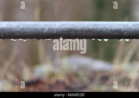 Regentropfen hängen unter einem Metallgeländer, unscharfen Hintergrund, außerhalb Stockfoto