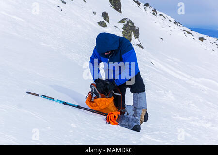 Wanderer in Winterkleidung, stehend auf einem schneebedeckten Hang prüft seine Ausrüstung vor dem Aufstieg auf den Berg Stockfoto