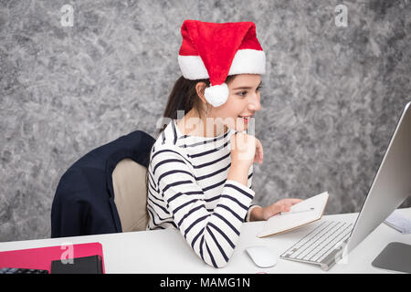 Schöne junge Mädchen mit einem santa Mütze im Büro für die festliche Jahreszeit Stockfoto