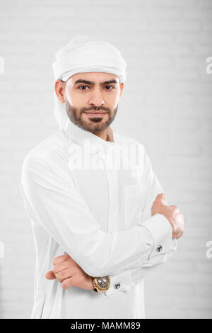 Vertikaler reichen reichen schönen erfolgreichen muslimischen Mann in traditionelle islamische Kleidung posiert in der Nähe von weißen Wand in Photo Studio verwischt. Konzept der Erfolg, cryptocurrency und virtuelles Geld. Stockfoto