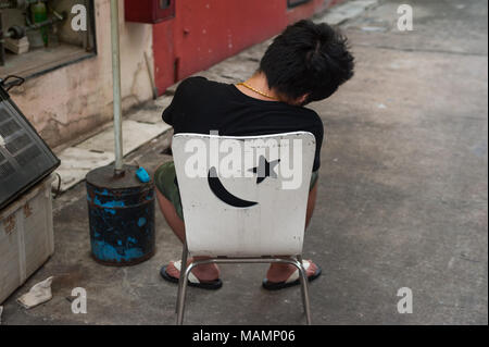 31.03.2018, Singapur, Republik Singapur, Asien - Ein junger Mann sitzt auf einem Stuhl in Singapur Chinatown und hält ein Nickerchen. Stockfoto