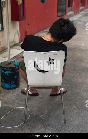 31.03.2018, Singapur, Republik Singapur, Asien - Ein junger Mann sitzt auf einem Stuhl in Singapur Chinatown und hält ein Nickerchen. Stockfoto