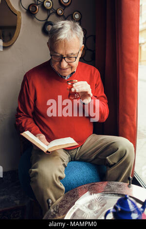 Älterer Mann sitzt im Cafe und liest ein Buch. Stockfoto