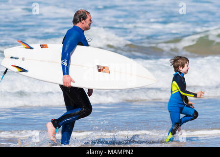 Ein Surfer seine surboard und läuft entlang der Küste mit seinen kleinen Sohn auf den Fistral Beach in Newquay Cornwall. Stockfoto