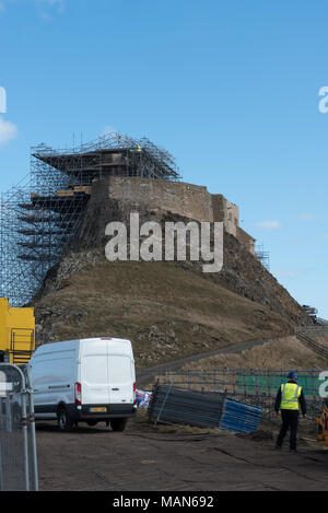 Lindisfarne Castle auf Holy Island, Northumberland, umgeben von Gerüsten während der Restaurierungsarbeiten unter bewölktem Himmel Stockfoto