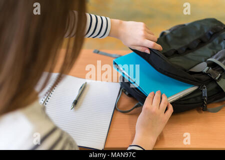 Junge Schülerin hinter ihrem Schreibtisch an der Klasse, ihre Lehrbücher aus dem Rucksack. Stockfoto