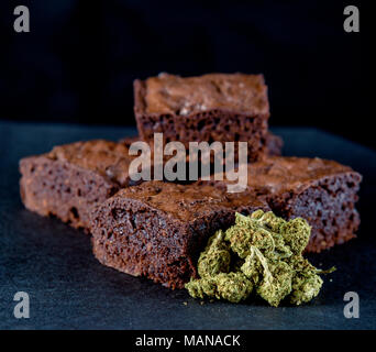 Ein Stapel von Marihuana genießbare Brownies neben einem kleinen Haufen medizinisches Marihuana nugs. Schwarzer Hintergrund Stockfoto