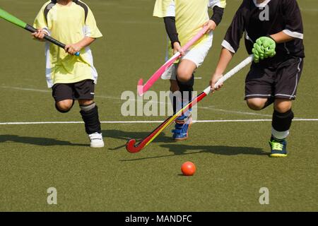 Kinder spielen Hockey konkurrierend. Zwei Mannschaftskameraden im Gelben Trikot Chase, die Player im schwarzen Uniform Stockfoto