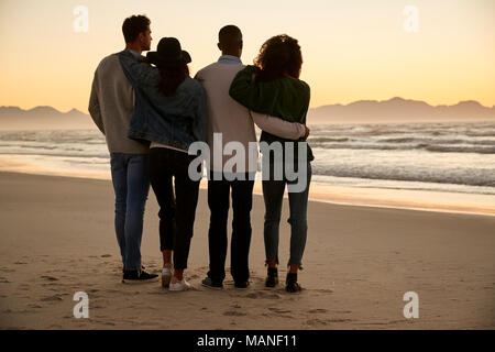 Eine Gruppe von Freunden im Winter Strand beobachten Sonnenaufgang zusammen Stockfoto