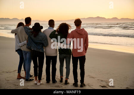 Eine Gruppe von Freunden im Winter Strand beobachten Sonnenaufgang zusammen Stockfoto