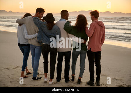 Eine Gruppe von Freunden im Winter Strand beobachten Sonnenaufgang zusammen Stockfoto