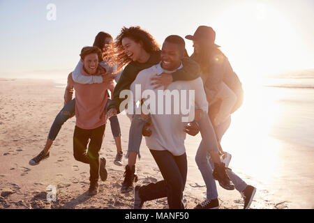 Eine Gruppe von Freunden mit Piggyback Rennen auf Winter Beach zusammen Stockfoto