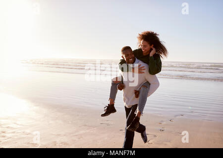 Mann, Frau, Huckepack auf Winter Urlaub am Strand Stockfoto