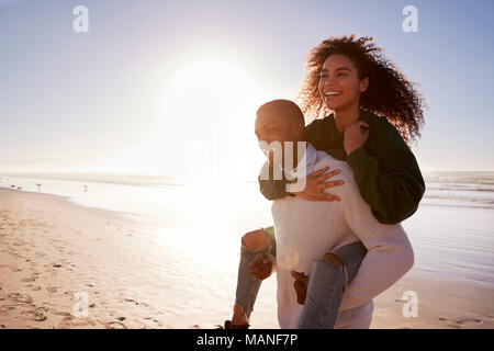 Mann, Frau, Huckepack auf Winter Urlaub am Strand Stockfoto