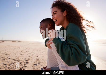 Mann, Frau, Huckepack auf Winter Urlaub am Strand Stockfoto