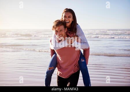 Mann, Frau, Huckepack auf Winter Urlaub am Strand Stockfoto