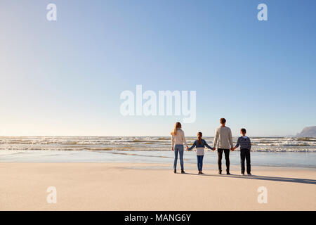 Ansicht der Rückseite des Familie im Winter Strand Hand in Hand mit Blick auf das Meer
