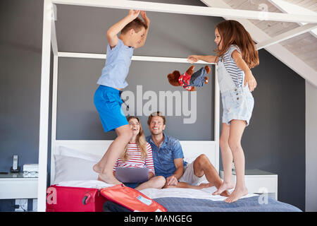 Begeistert Kinder springen auf dem Bett als Eltern Pack für Ferienhäuser Stockfoto