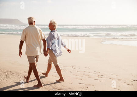 Ansicht der Rückseite des Senior Paar am Strand entlang zu laufen Hand in Hand Stockfoto