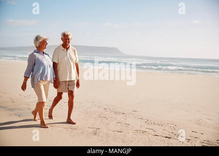 Älteres Rentnerehepaar Strand entlang gehen Hand in Hand Stockfoto