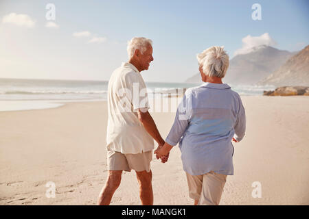 Ansicht der Rückseite des Senior Paar am Strand entlang zu laufen Hand in Hand Stockfoto