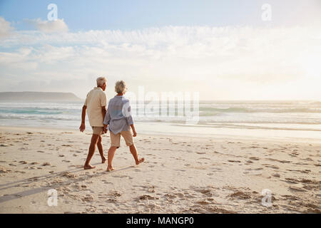 Ansicht der Rückseite des Senior Paar am Strand entlang zu laufen Hand in Hand Stockfoto