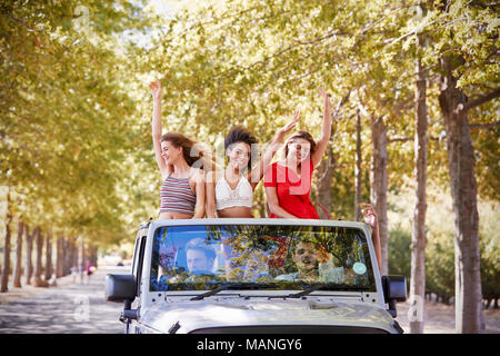Freundinnen in der Rückseite eines oben offenen Auto stehend winken Stockfoto