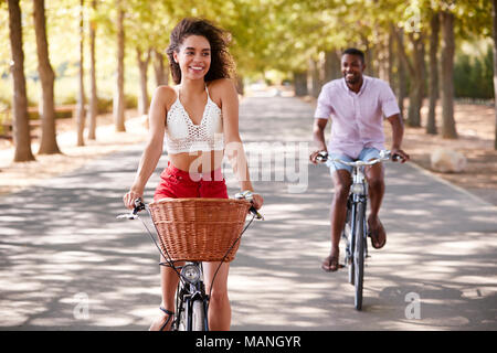 Junge Mixed Race Paar Fahrrad auf einer von Bäumen gesäumten Straße Stockfoto