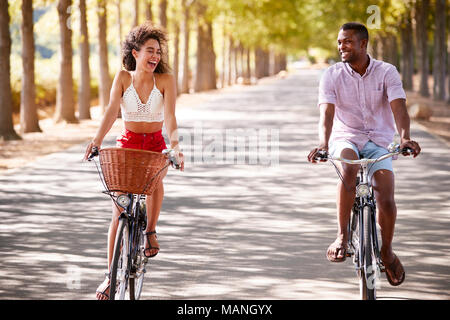 Lachen junges Paar auf dem Fahrrad über eine sonnige Straße Stockfoto