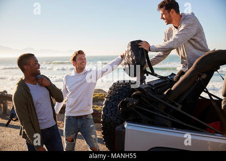 Drei junge Erwachsene männliche Freunde entladen Rucksäcke von Jeep Stockfoto