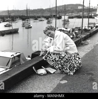 1950, historische, eine gut gekleidete Dame im Urlaub am Hafen knien streichelte eine lokale Cat, England, Großbritannien Stockfoto