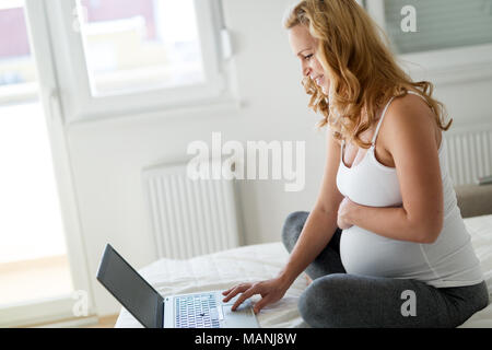 Gerne schwangere Frau mit Laptop im Schlafzimmer Stockfoto