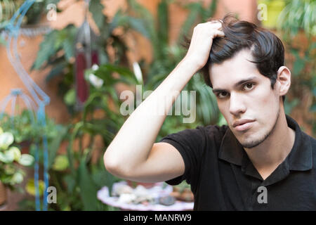 Porträt eines jungen Mannes im Freien mit seiner Hand auf seinen Haaren an Kamera, denken suchen und ernst. Stockfoto