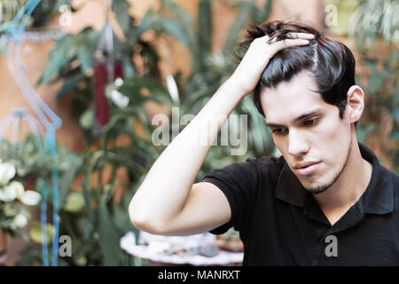 Porträt eines jungen Mannes im Freien mit der Hand auf seine Haare nach unten schauen, Denken und ernst. Stockfoto