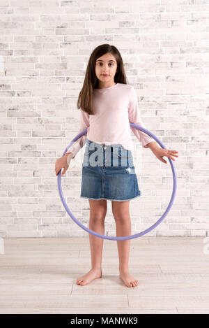 Junge hübsche Mädchen barfuß in legere Kleidung barfuß Posing beim Spielen mit einem Hula Hoop drinnen in einem hellen, luftigen Raum mit Mauer aus Stein und Holz Flo Stockfoto