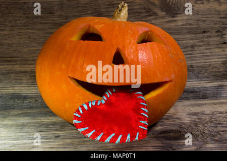 Kürbis für Halloween hält in seinem Mund ein rotes Herz für Valentinstag auf hölzernen Hintergrund Stockfoto