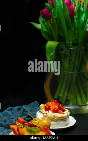 Tulip Vase mit Tasse Kaffee und Obst Kuchen auf dunklem Hintergrund. Kaffee Zeit. Blume Geschenk. Pavlova Cream pie Stockfoto