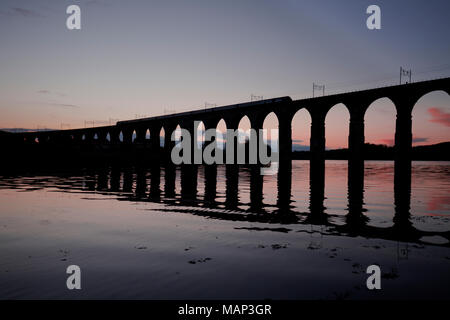 Eine länderübergreifende Züge Intercity 125 Kreuzung die Royal Border Bridge, Berwick upon Tweed mit der Silhouette im Wasser bei Sonnenuntergang widerspiegelt. Stockfoto