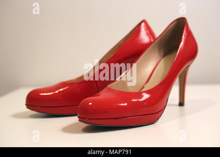 Ein Stil leben von ein paar High Heels auf einem weißen Tisch. Schuhe sind Rot glänzende Schuhe aus Leder und der Hintergrund ist weiß. Stockfoto