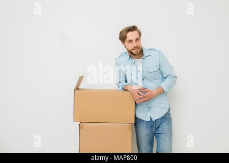 Blonder Mann mit Bart ständigen entspannt Neben seine Sachen in Kartons verpackt, whaiting für jemand, sie zu tragen, auf weißem Hintergrund Stockfoto