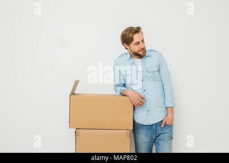 Blonder Mann mit Bart ständigen entspannt Neben seine Sachen in Kartons verpackt, whaiting für jemand, sie zu tragen, auf weißem Hintergrund Stockfoto