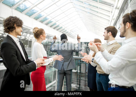 Zwei Geschäftsleute die Hände schütteln, während ihre Kollegen applaudierten und lächelnd Stockfoto