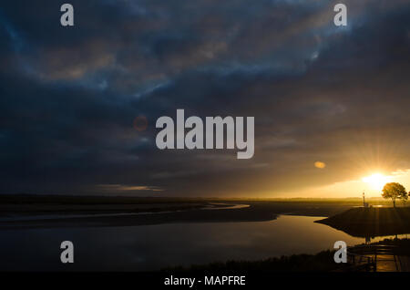Goldener Sonnenuntergang über ruhigen Mündungsgewässern in Saint-Valery-sur-Somme, Frankreich, mit dramatischem blaugrauem Himmel und friedlichen Reflexen. Stockfoto