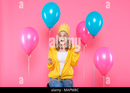 Funny Girl in Geburtstag hat, Luftballons und Ausblasen Horn auf Pastell rosa Hintergrund. Attraktive trendige Teenager feiert Geburtstag. Stockfoto