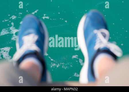 Teal Wasser & Füße in blau Sneakers (unscharf) nach unten hängen. Stockfoto