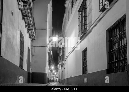 Monochrome eines Night Street Scene/Blick auf eine schmale Straße mit Kopfsteinpflaster im Barrio/Bezirk Santa Cruz in Sevilla 2018, Andalusien, Spanien Stockfoto