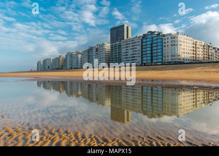 Reflexion der Städtischen Skyline von Ostende durch die Nordsee Strand mit Blick über die Strandpromenade bei Sonnenuntergang, Westflandern, Belgien. Stockfoto